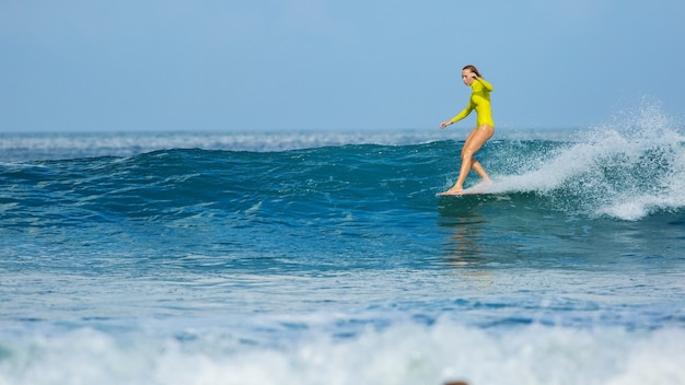 Hermosa chica surfista monta un longboard y hace un truco de paseo en la nariz.