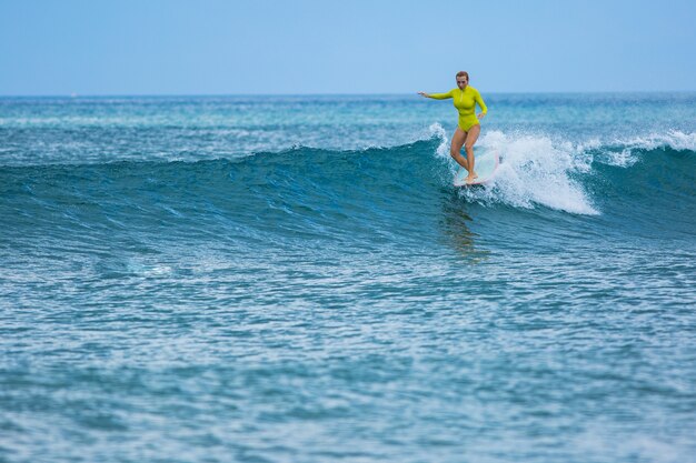 Hermosa chica surfista monta un longboard y hace un truco de paseo en la nariz.