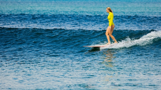 Hermosa chica surfista monta un longboard y hace un truco de paseo en la nariz.