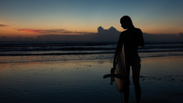 Hermosa chica con una tabla de surf al atardecer