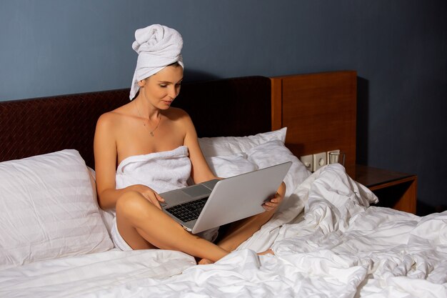 Hermosa chica trabaja en una computadora en la cama.