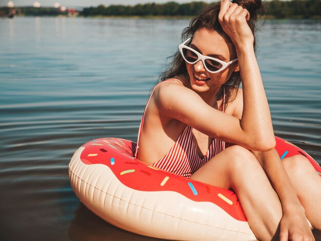 Hermosa chica en traje de baño flotando con una rosquilla inflable en el mar