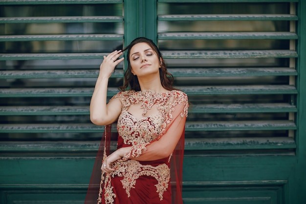 Una hermosa chica turca con un vestido largo rojo camina en la ciudad vieja de verano