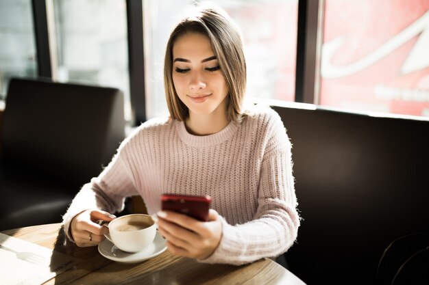 Hermosa chica usando su teléfono móvil en la cafetería durante el almuerzo de freno de café a diario