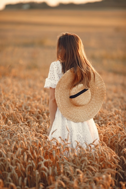 Hermosa chica con un vestido blanco. Mujer en un campo de otoño. Dama con sombrero de paja.