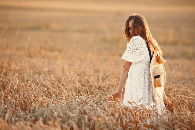 Hermosa chica con un vestido blanco. Mujer en un campo de otoño. Dama con sombrero de paja.