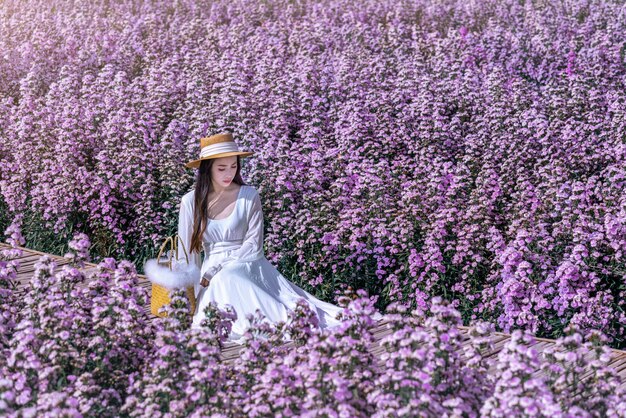 Hermosa chica en vestido blanco sentada en los campos de flores de Margaret