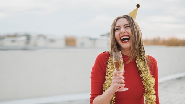 Hermosa chica en vestido rojo riendo en la azotea con copa de champán