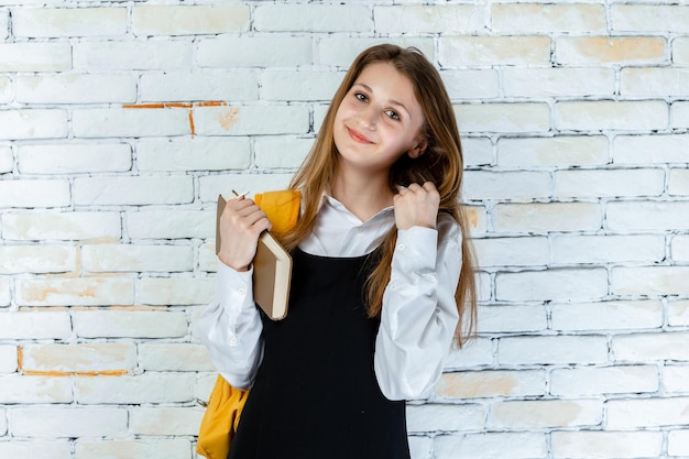 Hermosa colegiala de pie sobre fondo blanco y sosteniendo su libro