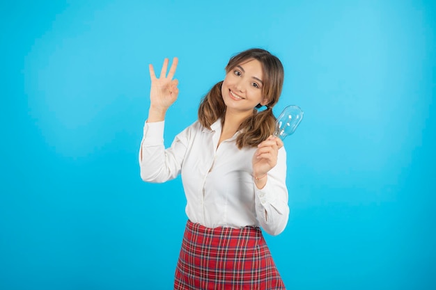 Hermosa colegiala sonriente sosteniendo una bombilla de idea y gesticulando tres. foto de alta calidad