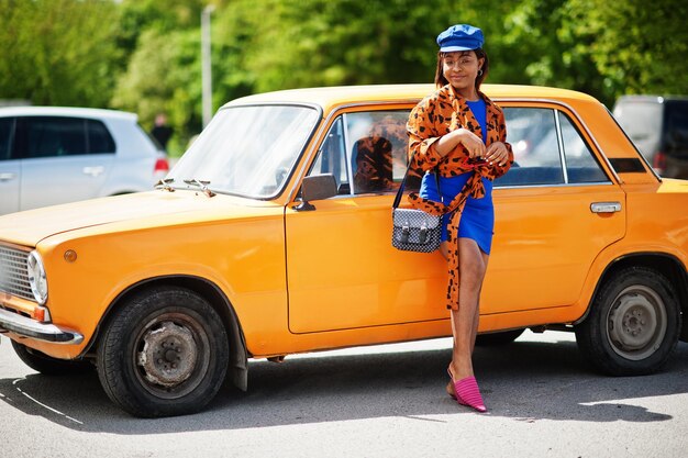 Hermosa dama afroamericana parada cerca de un auto retro clásico naranja