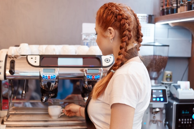Hermosa dama caucásica sonriendo preparando café caliente en la cafetería moderna