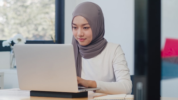 Hermosa dama musulmana asiática ropa casual trabajando con ordenador portátil en la nueva oficina normal moderna.