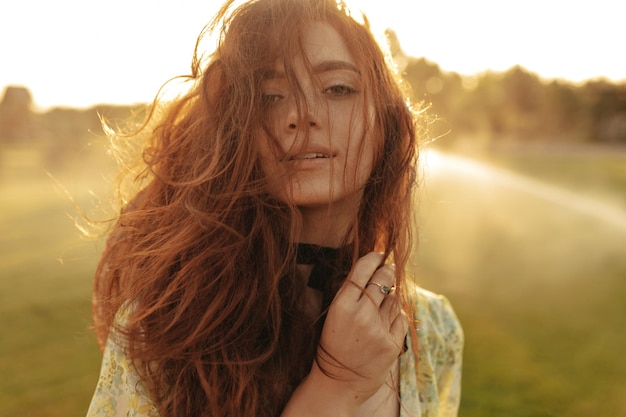 Hermosa dama con peinado ondulado astuto y vendaje negro fresco en el cuello con ropa de verano de moda mirando a la cámara al aire libre