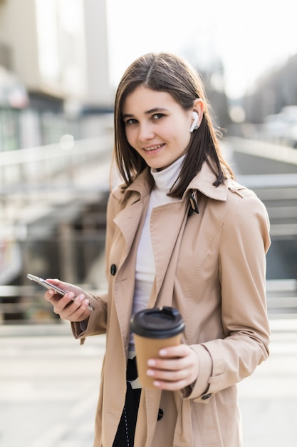 Hermosa dama toma café y lee noticias en su teléfono afuera