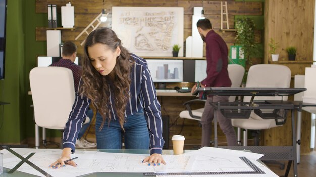 Hermosa diseñadora caucásica trabajando en planos en oficina moderna y acogedora