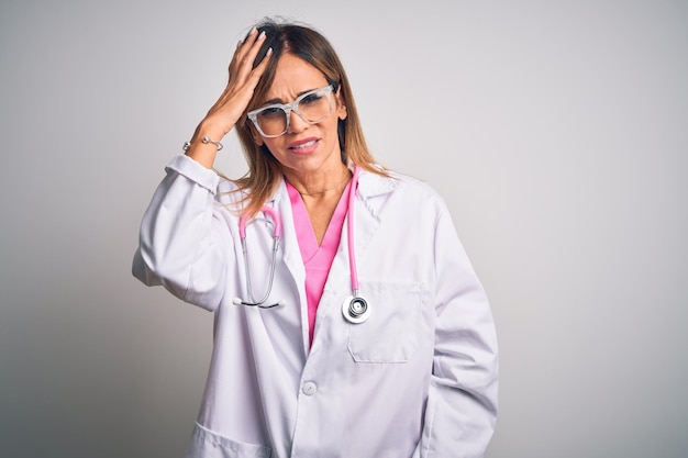 Foto gratuita hermosa doctora de mediana edad con estetoscopio rosa sobre fondo blanco aislado confundida y preguntada sobre la pregunta incierta con duda pensando con la mano en la cabeza concepto pensativo