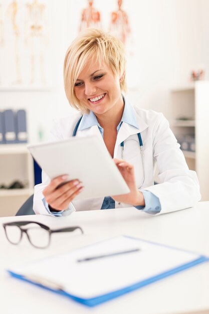 Hermosa doctora sonriente con tableta digital en la oficina