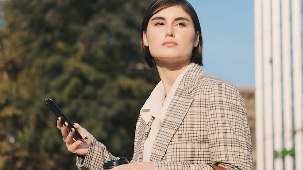 Hermosa y elegante mujer de negocios que trabaja en un teléfono inteligente esperando una reunión de negocios en el centro