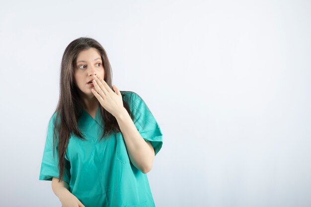 Hermosa enfermera sorprendida sosteniendo su mano a su boca y mirando a otro lado.