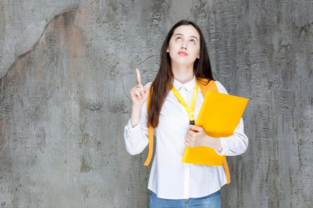 Hermosa estudiante con camisa blanca sosteniendo un libro y señalando. foto de alta calidad