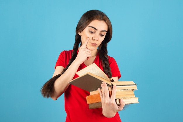 Hermosa estudiante en camiseta roja leyendo atentamente el libro sobre la pared azul.