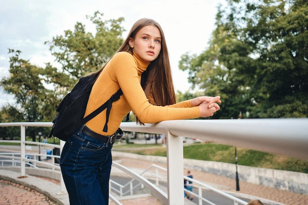 Hermosa estudiante casual con mochila mirando atentamente hacia otro lado en el parque de la ciudad