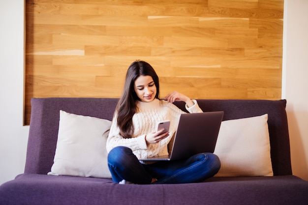 Hermosa estudiante feliz trabajando en una computadora portátil sentado en la cama en la casa