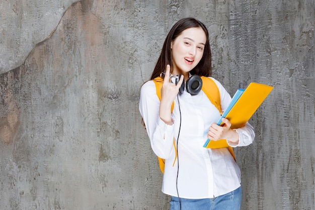 Hermosa estudiante con mochila y auriculares que muestran signos. foto de alta calidad