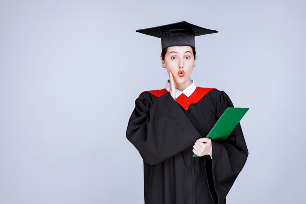 Hermosa estudiante de posgrado con diploma de pie boca abierta. Foto de alta calidad