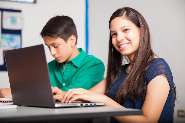 Hermosa estudiante de secundaria hispana usando una computadora portátil en un salón de clases