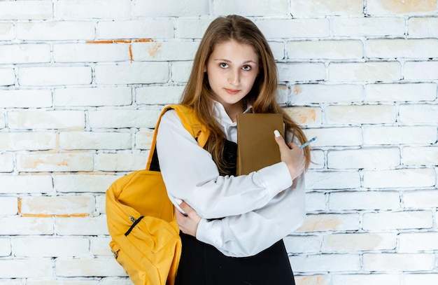 Una hermosa estudiante en uniforme se para sobre un fondo blanco y abraza su libro Foto de alta calidad