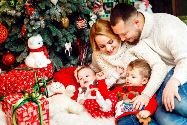 Hermosa familia con niños en cálidos suéteres posa ante una pared verde y rico árbol de Navidad