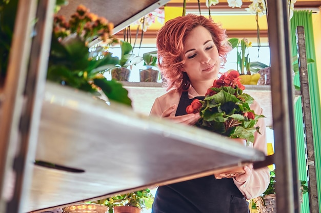 Hermosa florista pelirroja con uniforme trabajando en una floristería.