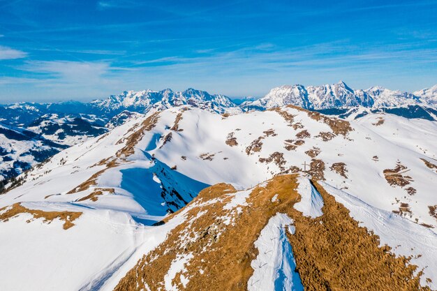 Hermosa foto de los Alpes cubiertos de nieve con una cruz en uno de los picos bajo un cielo azul