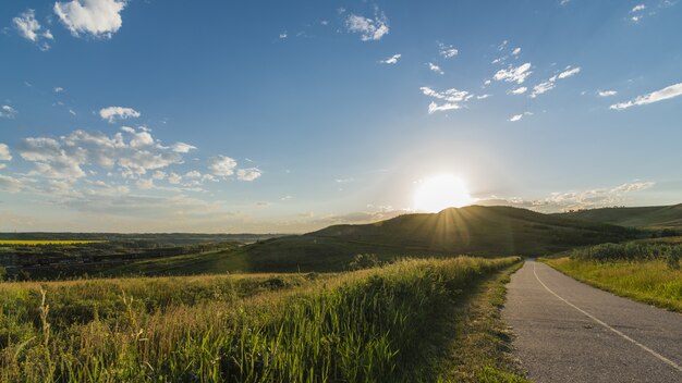 Hermosa foto de una carretera cerca de hierba y montañas con un cielo despejado