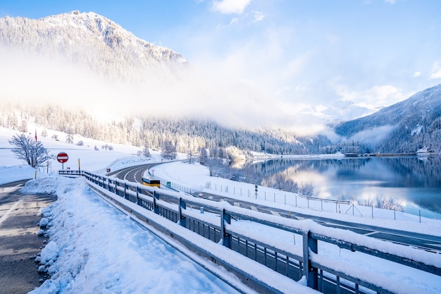 Hermosa foto de una carretera cerca de un lago rodeado de montañas cubiertas de nieve.