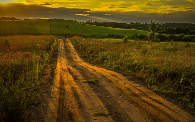 Hermosa foto de una carretera a través del campo durante la impresionante puesta de sol
