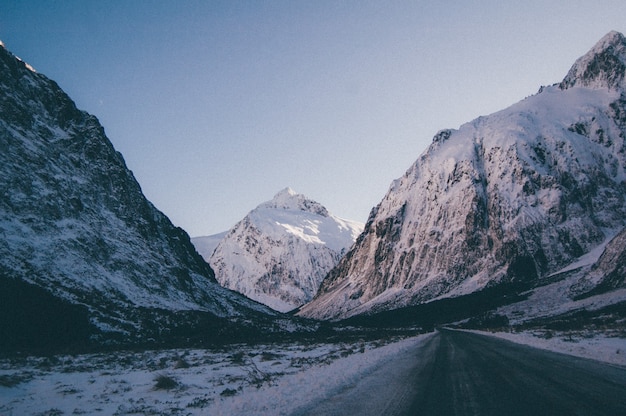Hermosa foto de una carretera vacía atravesando altas montañas rocosas cubiertas de nieve