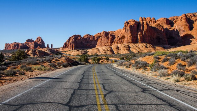 Hermosa foto de una carretera vacía en medio de un desierto con arbustos y acantilados en la distancia