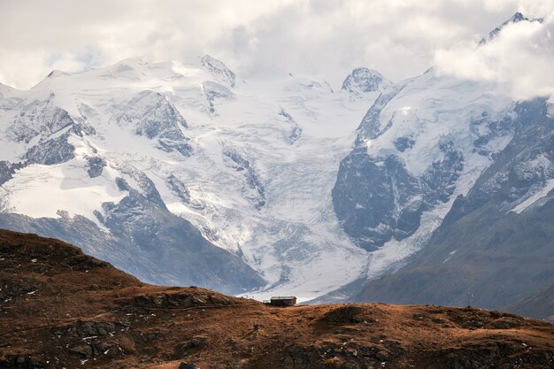 Hermosa foto de una casa al borde del acantilado con montañas nevadas