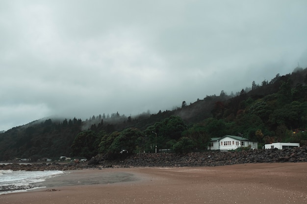 Hermosa foto de una casa solitaria en una playa de niebla con un hermoso bosque detrás - Concepto de horror