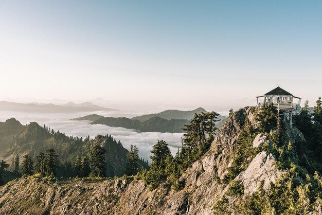 Hermosa foto de un cenador blanco en la cima de la montaña cerca de los árboles con un cielo despejado en segundo plano.