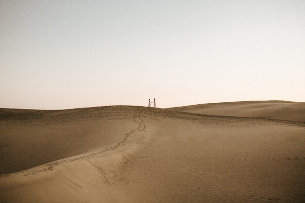 Hermosa foto de una colina del desierto con dos hembras cogidos de la mano en la cima en la distancia