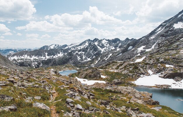 Hermosa foto de colinas cubiertas de hierba con rocas y estanques cerca de las montañas bajo un cielo nublado