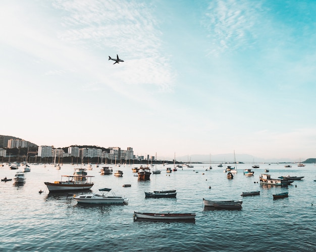 Hermosa foto de la costa de una ciudad costera urbana con muchos barcos y un avión volando en el cielo