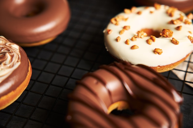 Hermosa foto de deliciosas donas cubiertas con el glaseado de chocolate blanco y marrón sobre una mesa negra