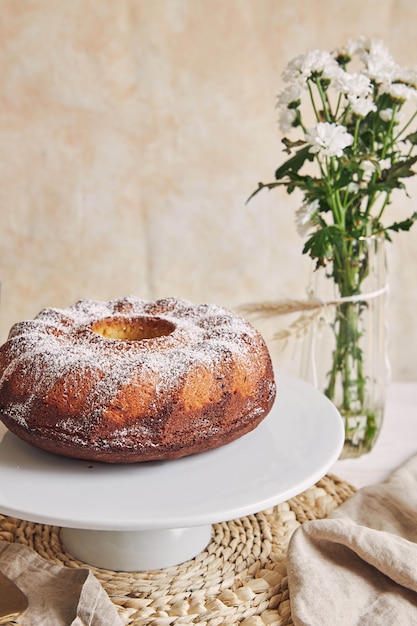 Hermosa foto de un delicioso pastel de anillo puesto en un plato blanco y una flor blanca cerca de él