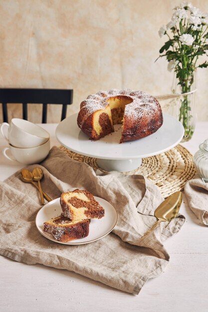 Hermosa foto de un delicioso pastel de anillo puesto en un plato blanco y una flor blanca cerca de él