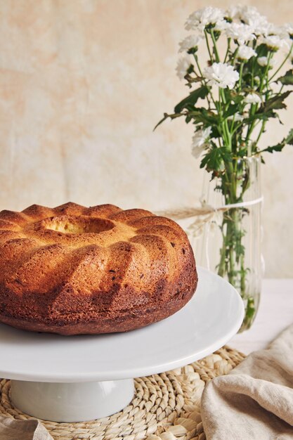 Hermosa foto de un delicioso pastel de anillo puesto en un plato blanco y una flor blanca cerca